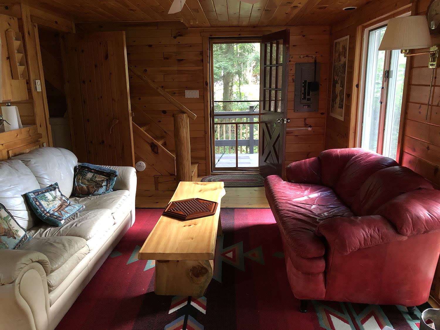 A couch faces a red chair on a red carpet in a wood paneled room