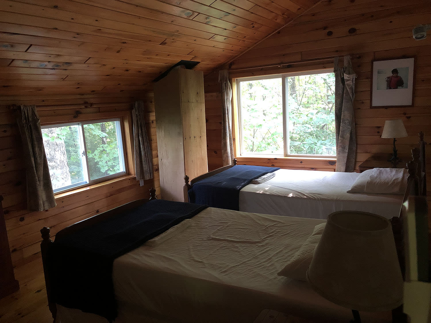 Two white beds with blue blankets at the bottom in a wood paneled room