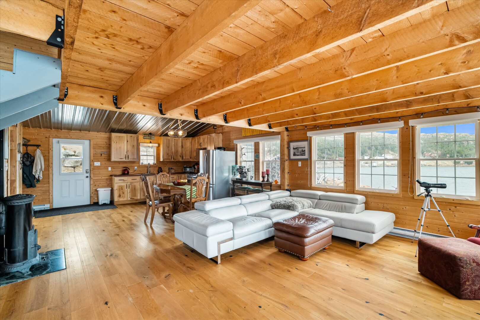 Sunlit interior with wood beams, large windows, and cozy seating overlooking the water