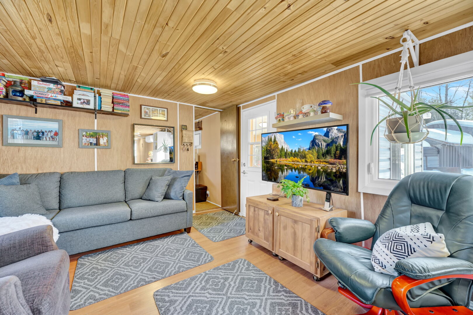A wood-paneled living room with a grey couch and grey rugs