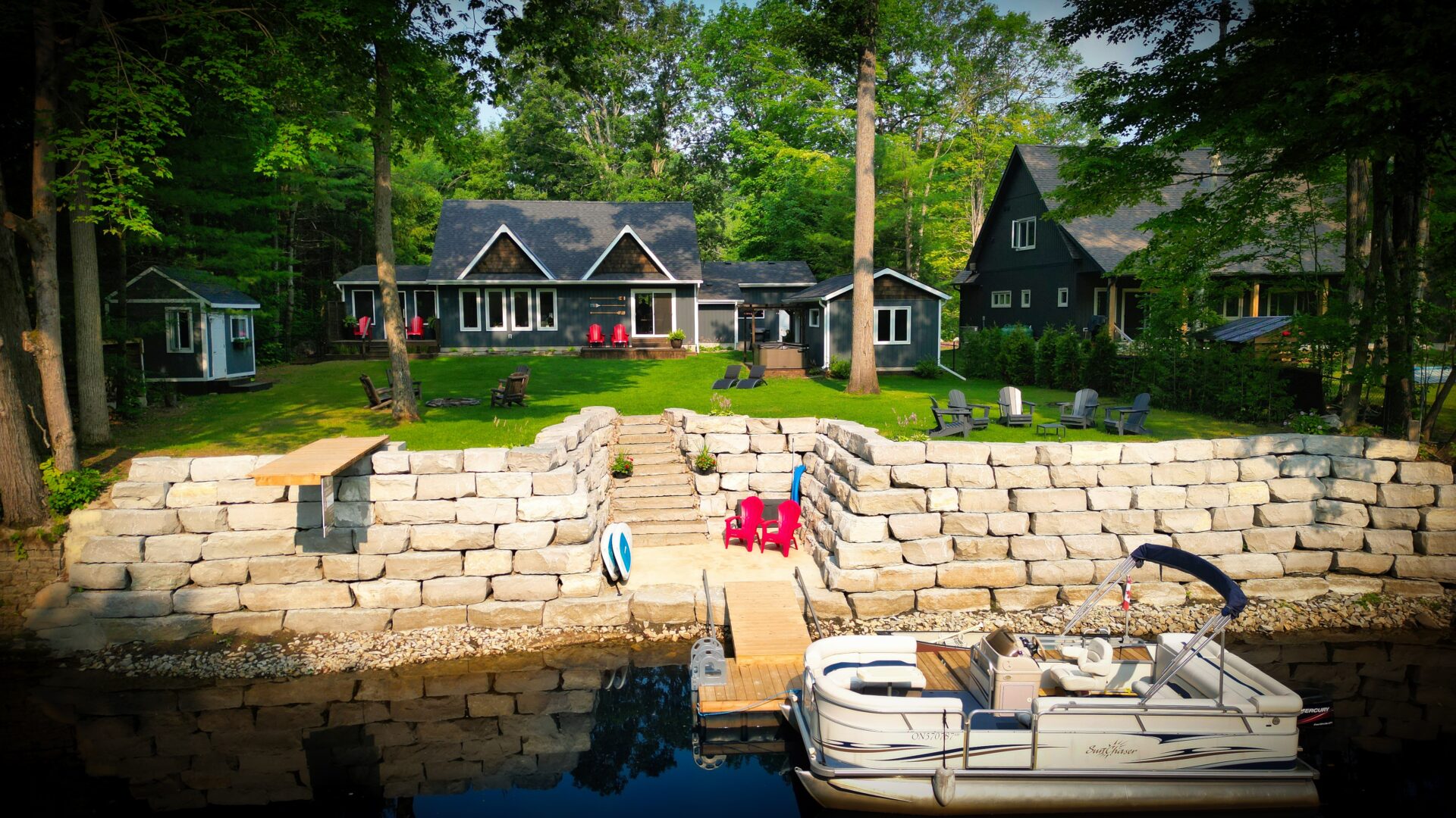 A blue-grey cottage on a vibrant green lawn. In front, a stone wall and small dock