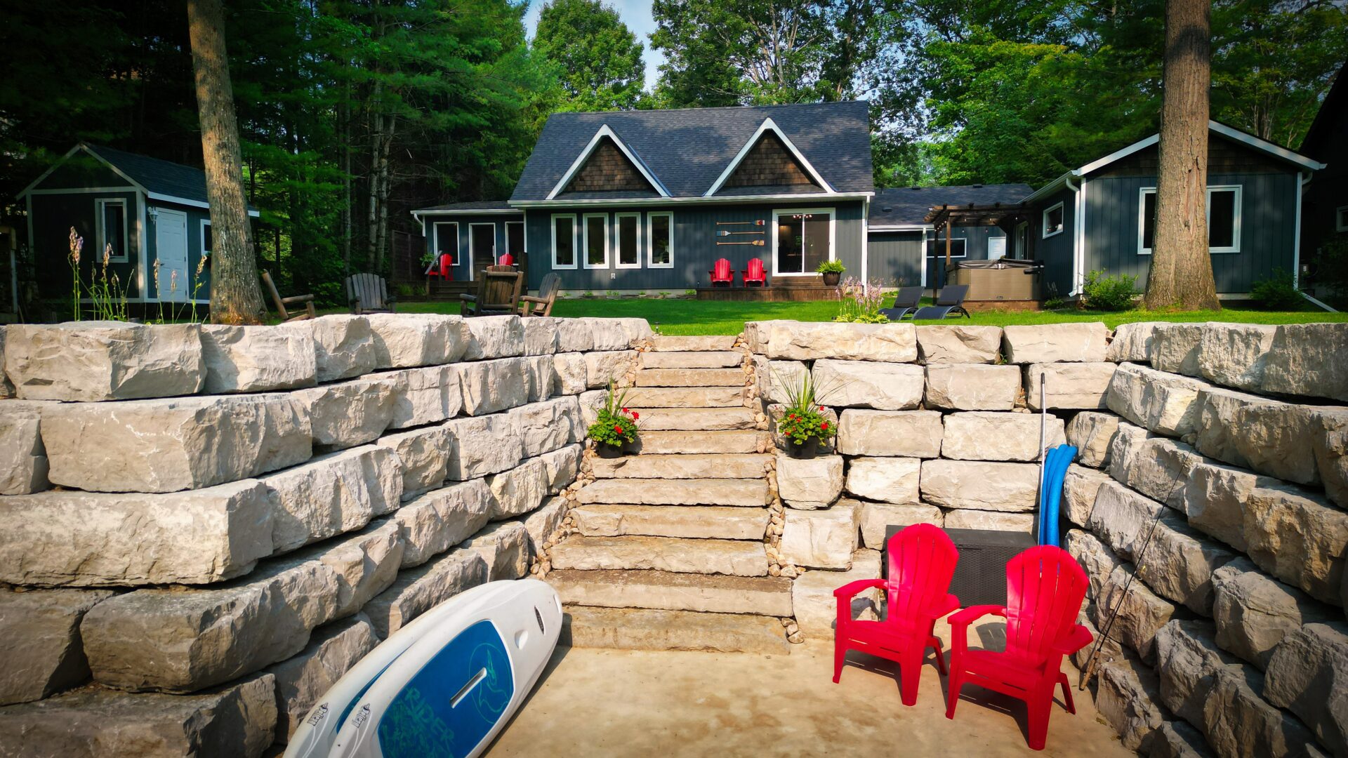 A dock with a kayak and two red Muskoka chairs