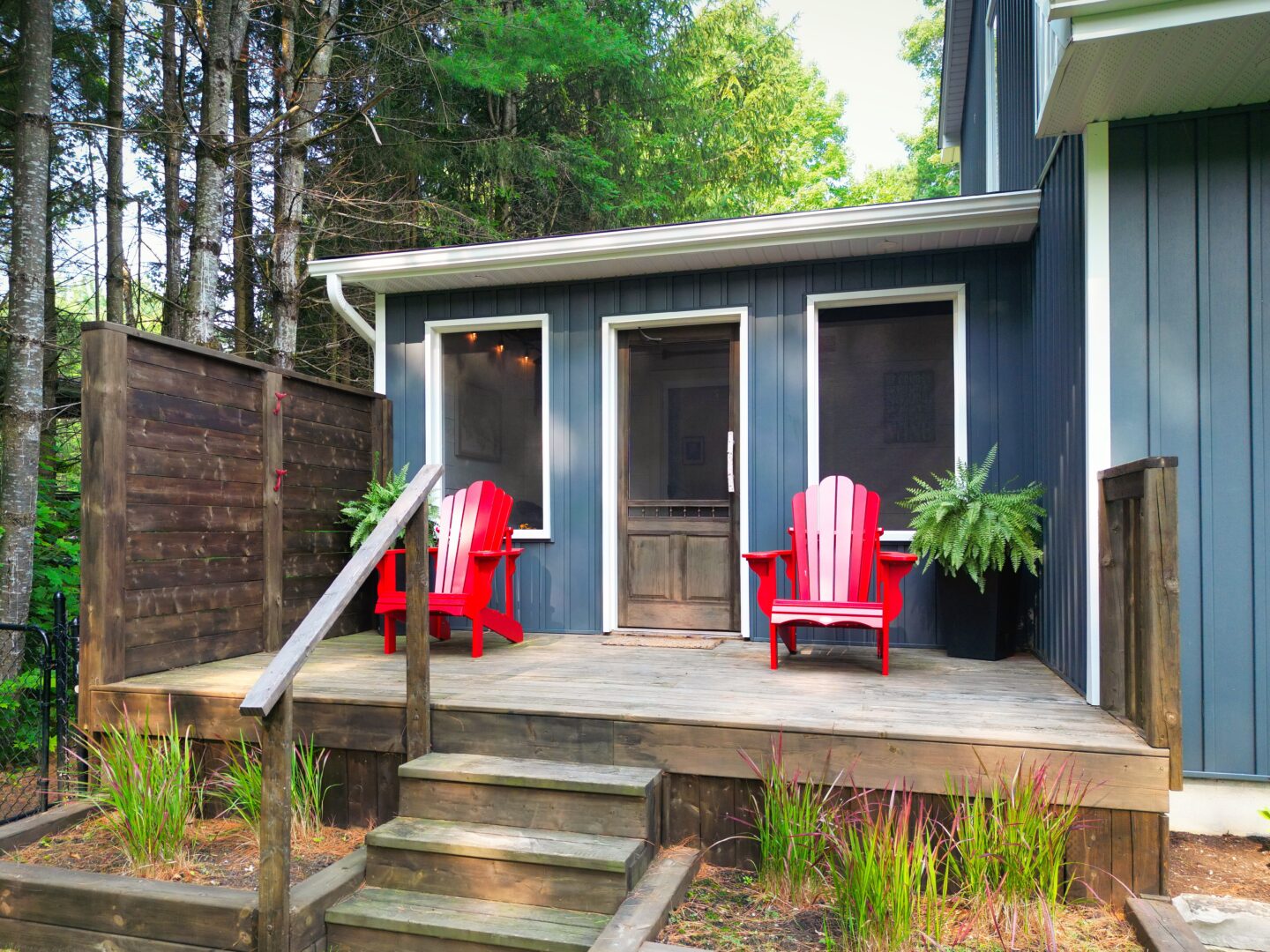 A blue-grey cottage with red Muskoka chairs framing the door