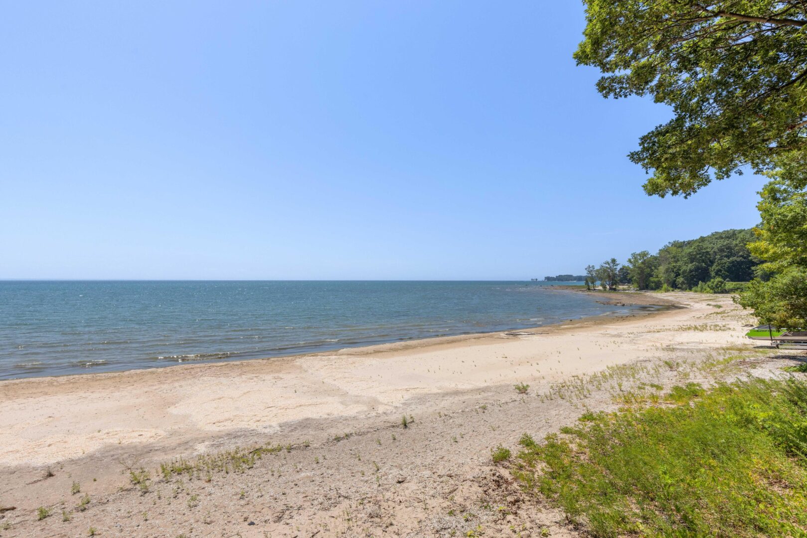 Secluded stretch of white sand beach with clear blue water and treed shoreline on Lake Erie