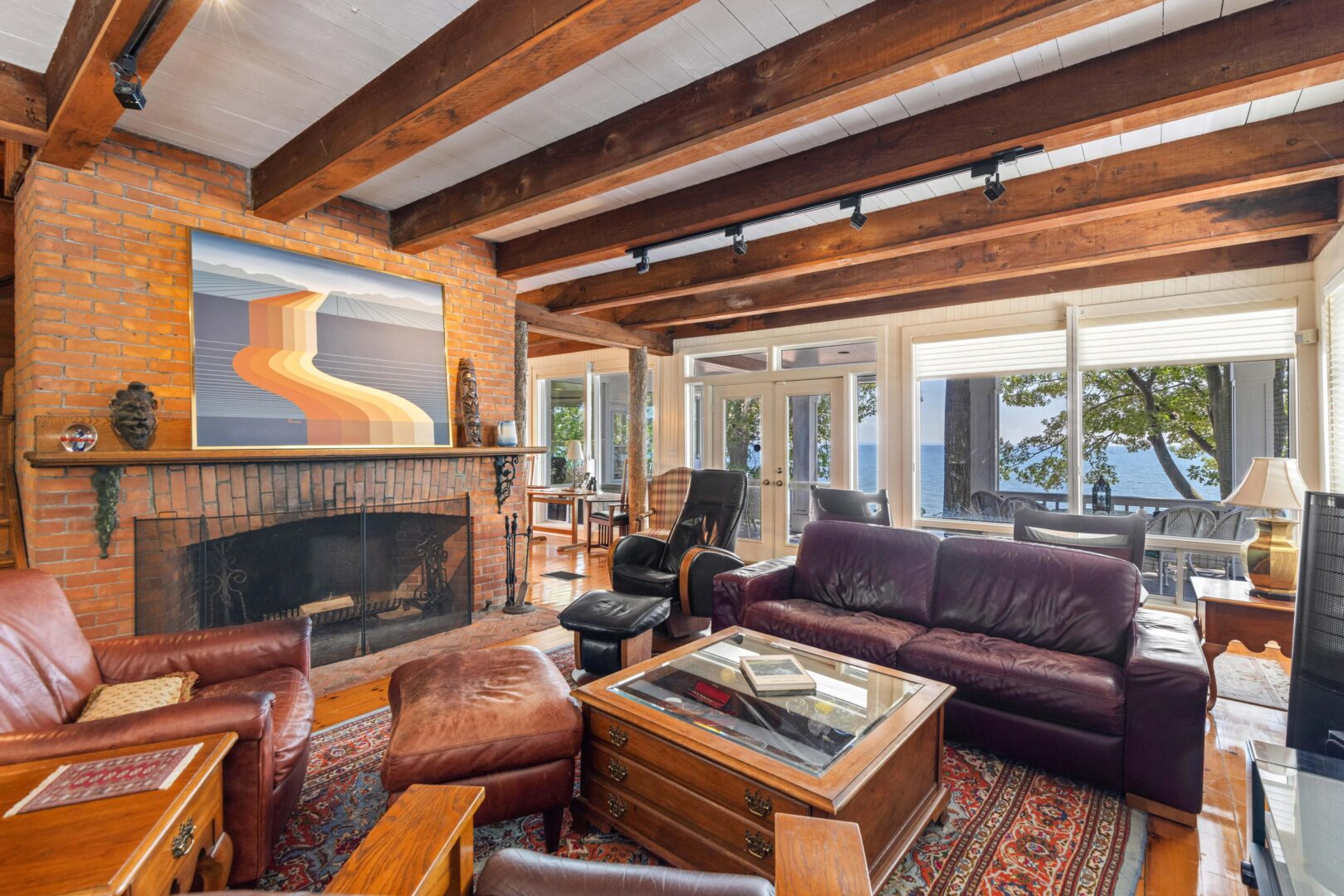 Warm, rustic living area featuring exposed wood beams, leather furniture, and a brick fireplace