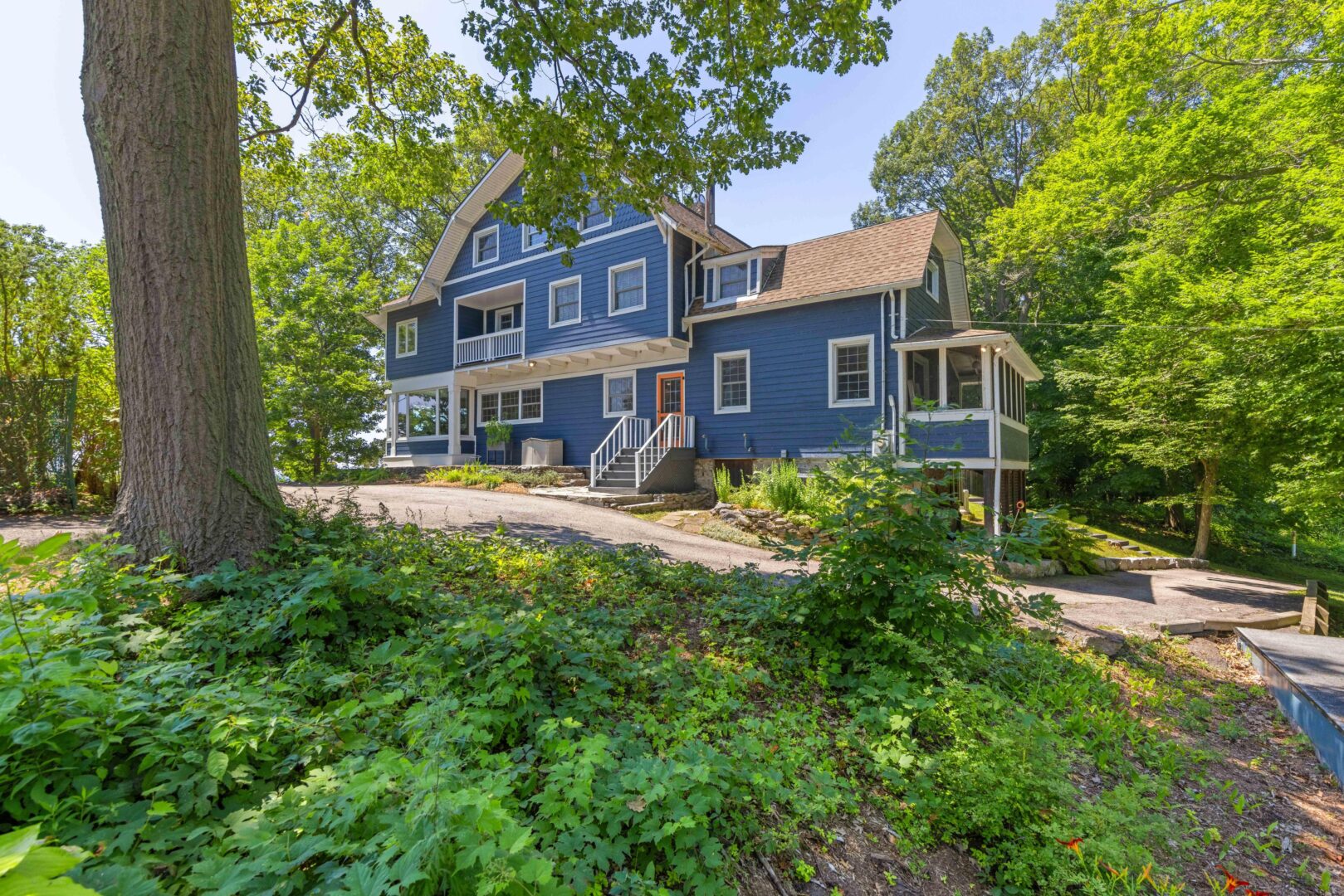 View of the historic home's front façade with wood siding, set against a wooded slope and landscaped grounds