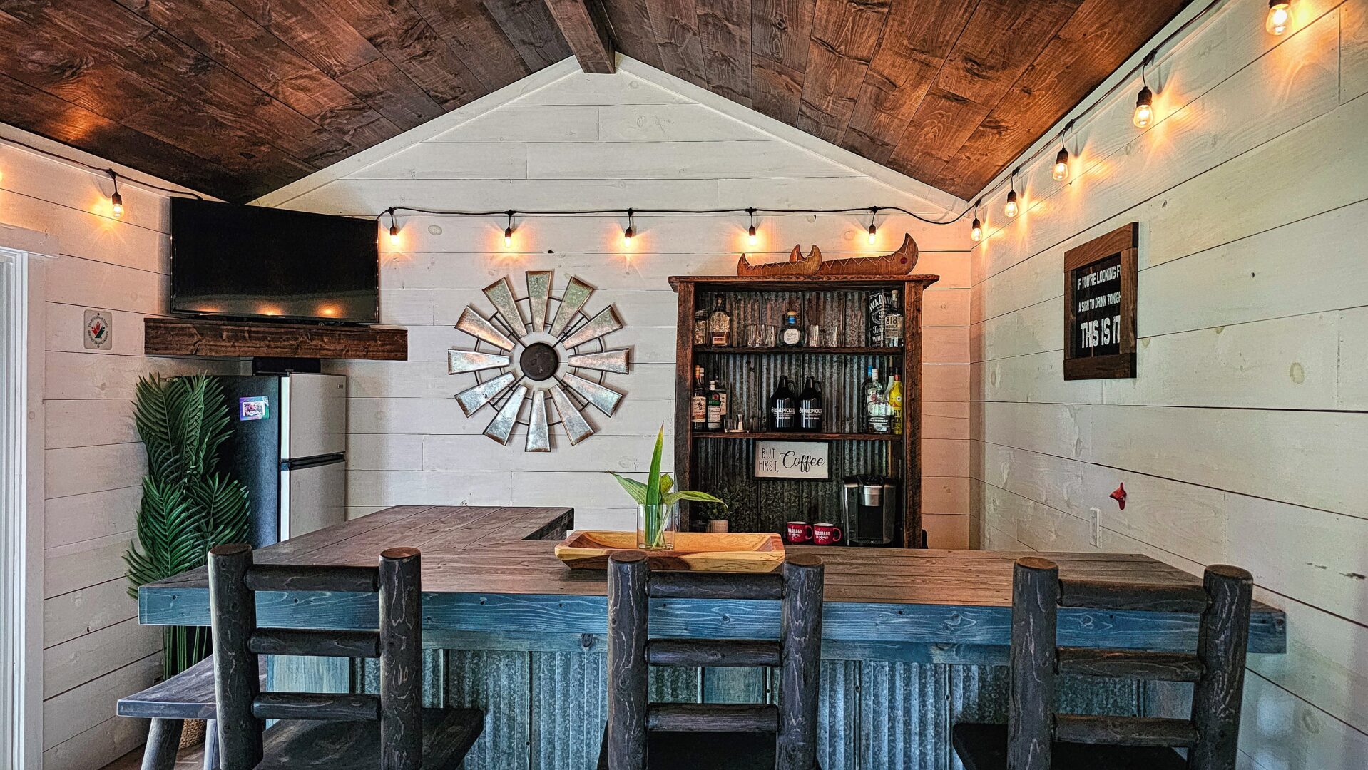 A home bar. Behind, a white wall with a built-in shelf of bottles