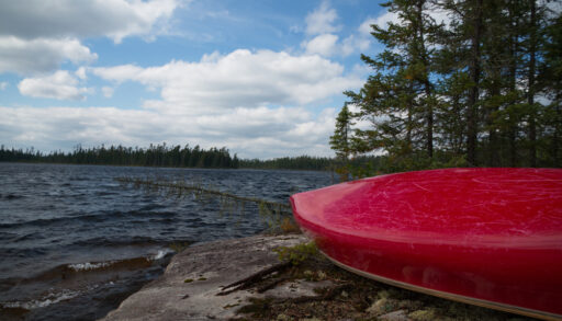 Red tandem canoe upside down on a rocky shore