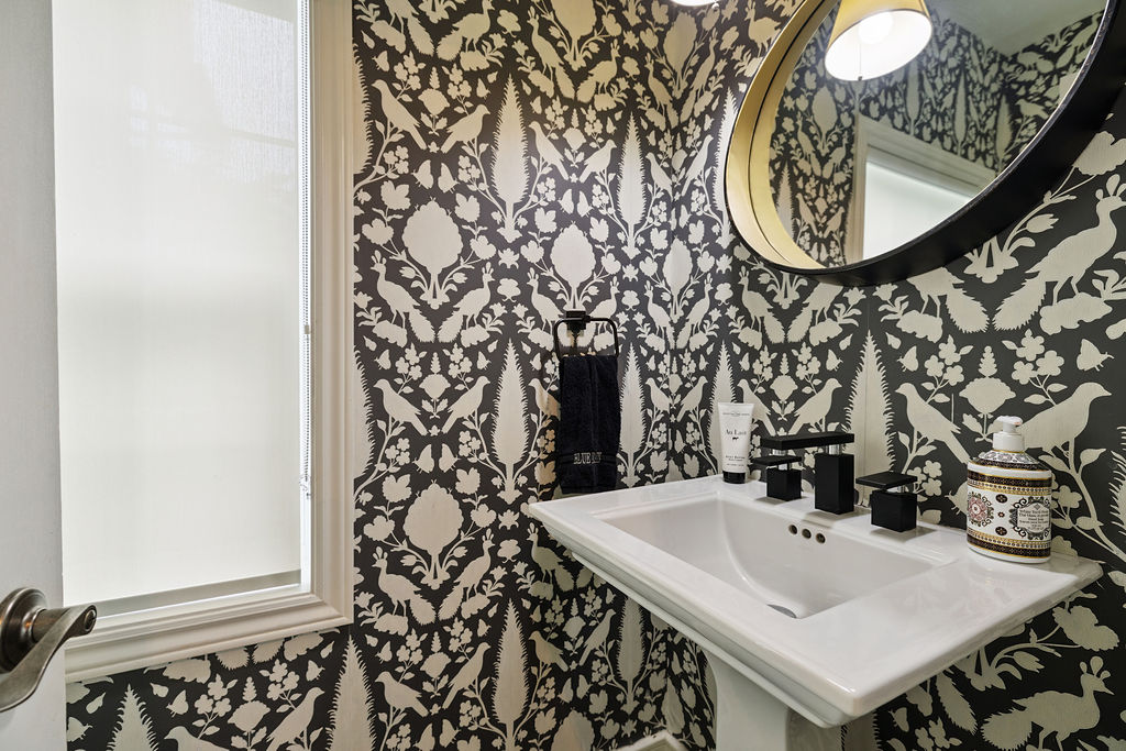 A black and white wallpapered powder room with a white sink