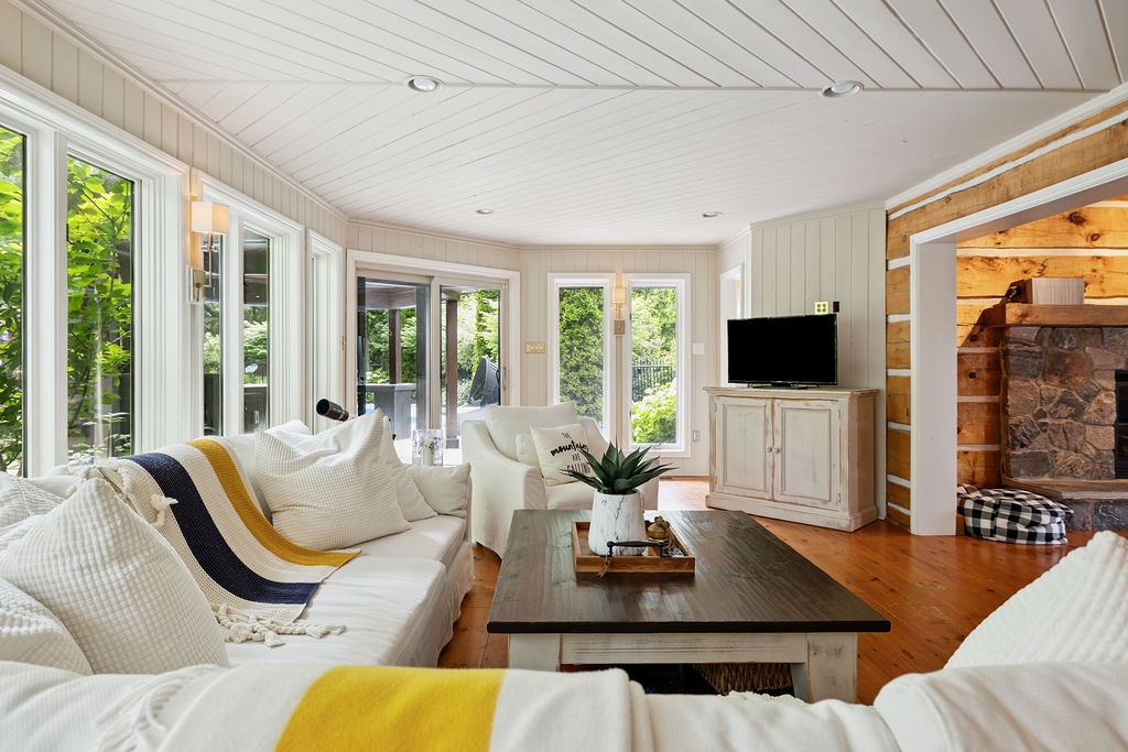 An L-shaped white couch faces a small rectangular coffee table in a white wood paneled room