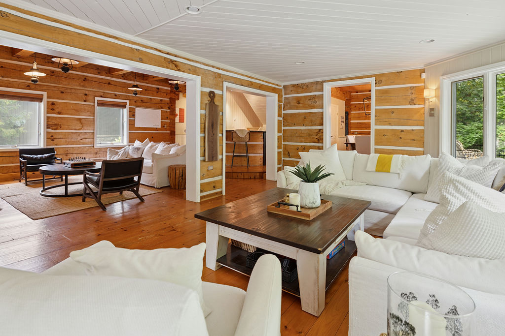 An L-shaped white couch faces a small rectangular coffee table in a white wood paneled room