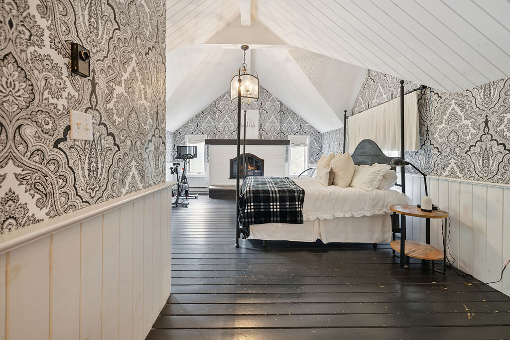 A spacious black and white bedroom with cathedral ceilings and a white fireplace