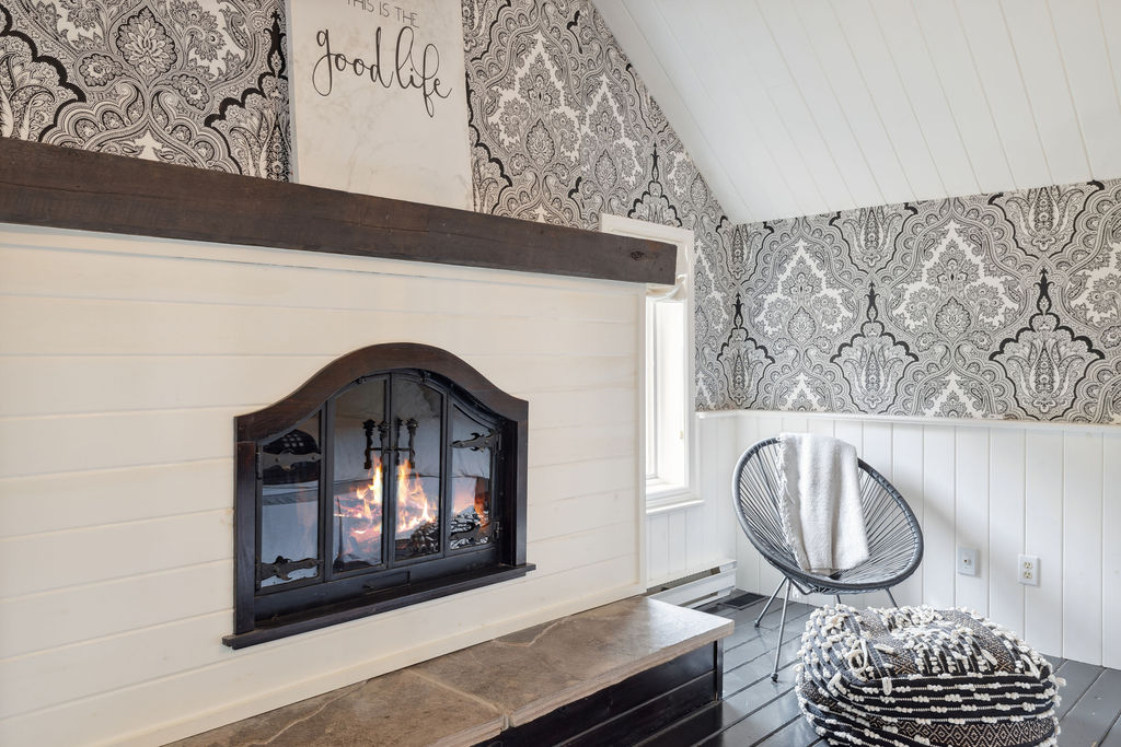 A white fireplace with brown trim in a bedroom with black-and-white wallpaper