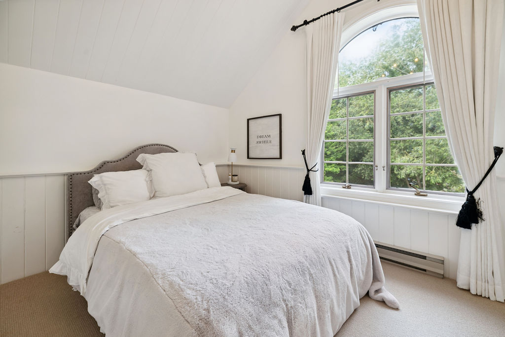 A white bed in a white bedroom with a large window