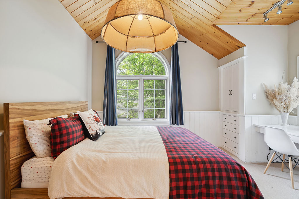 A white bed with a plaid throw blanket in a white room