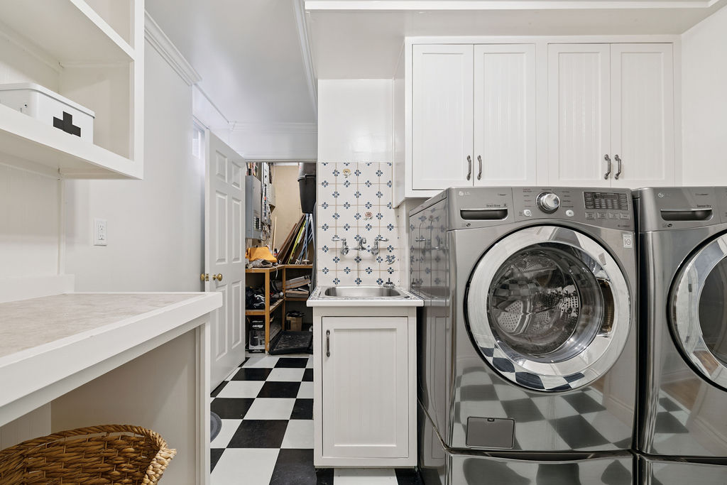 A white laundry room with silver laundry machines and black-and-white checkered floors