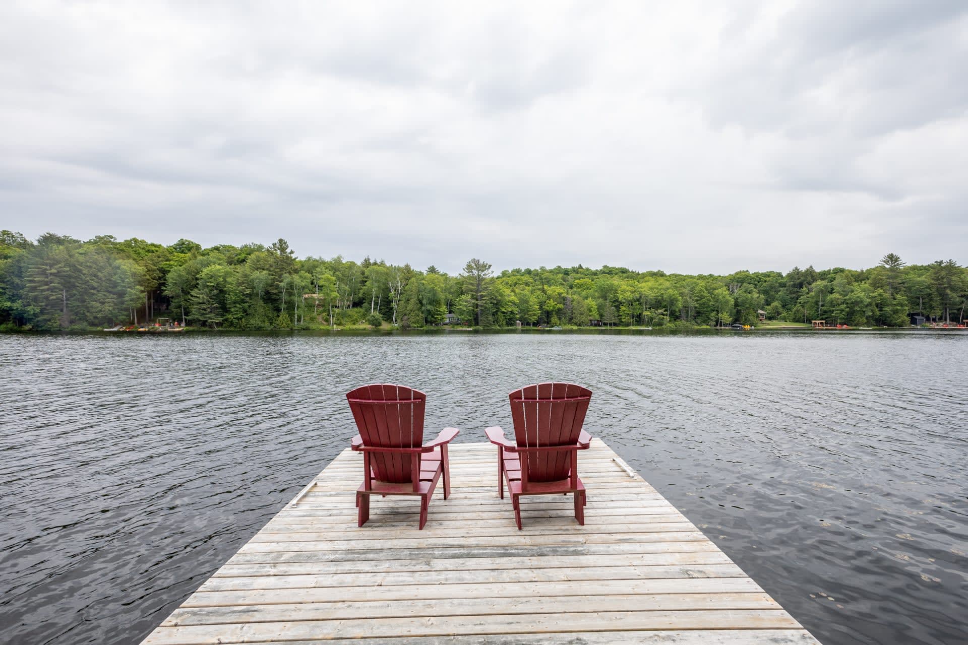 Two red Muskoka chairs at the end of a dock