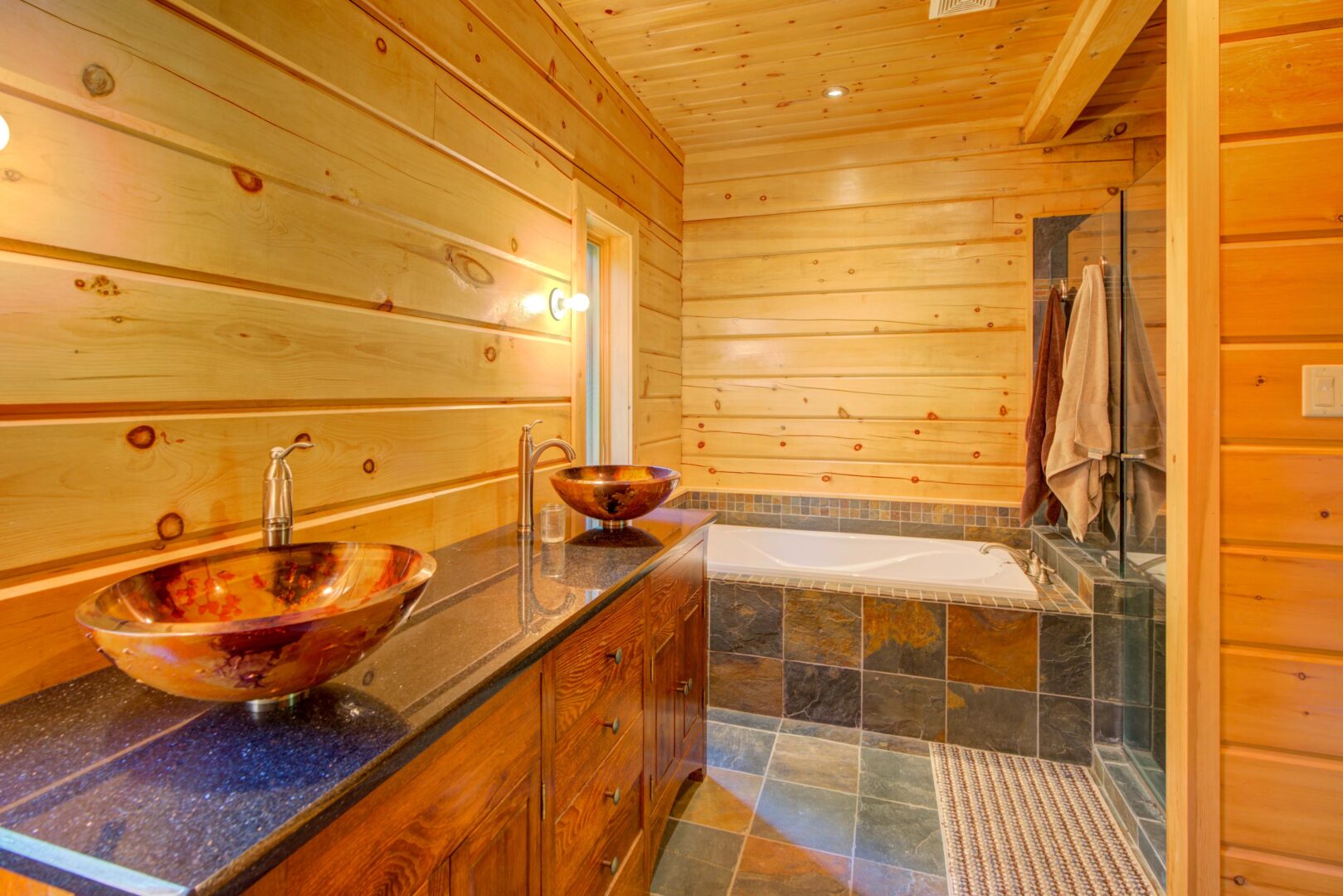 A wood vanity next to a stone bathtub in a wood paneled bathroom