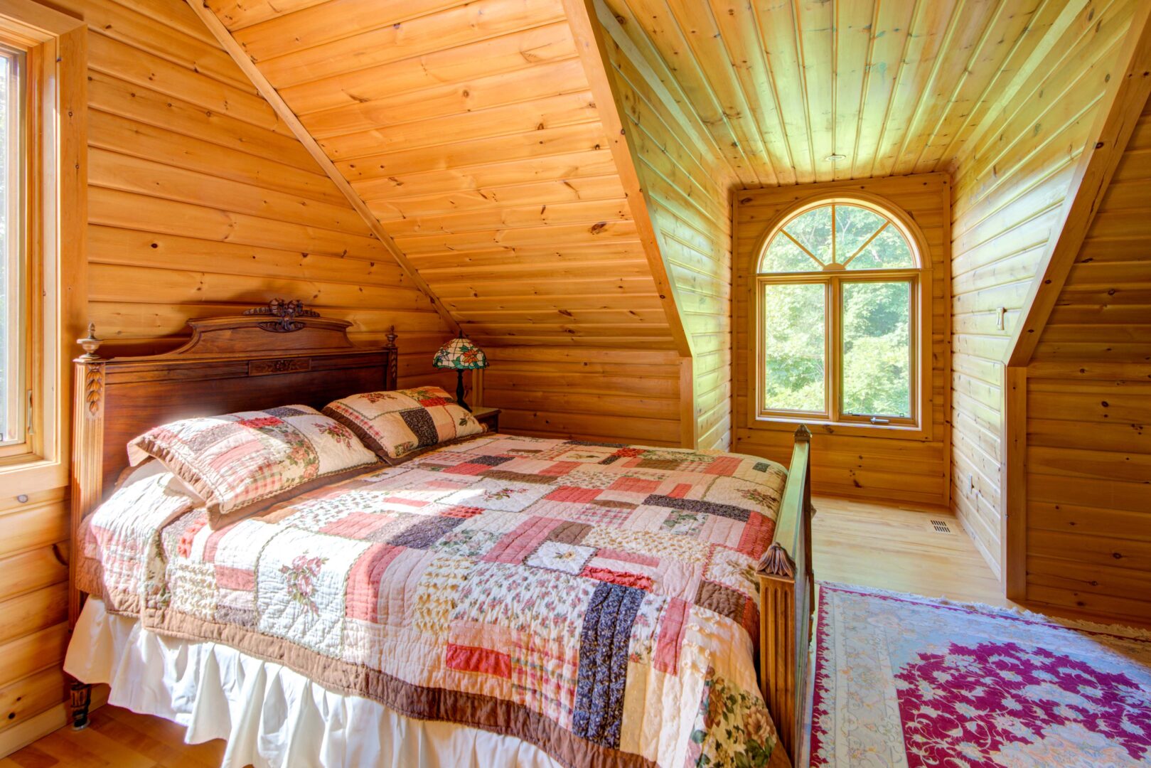 A bright quilt on a wood bed in an angled wood paneled room