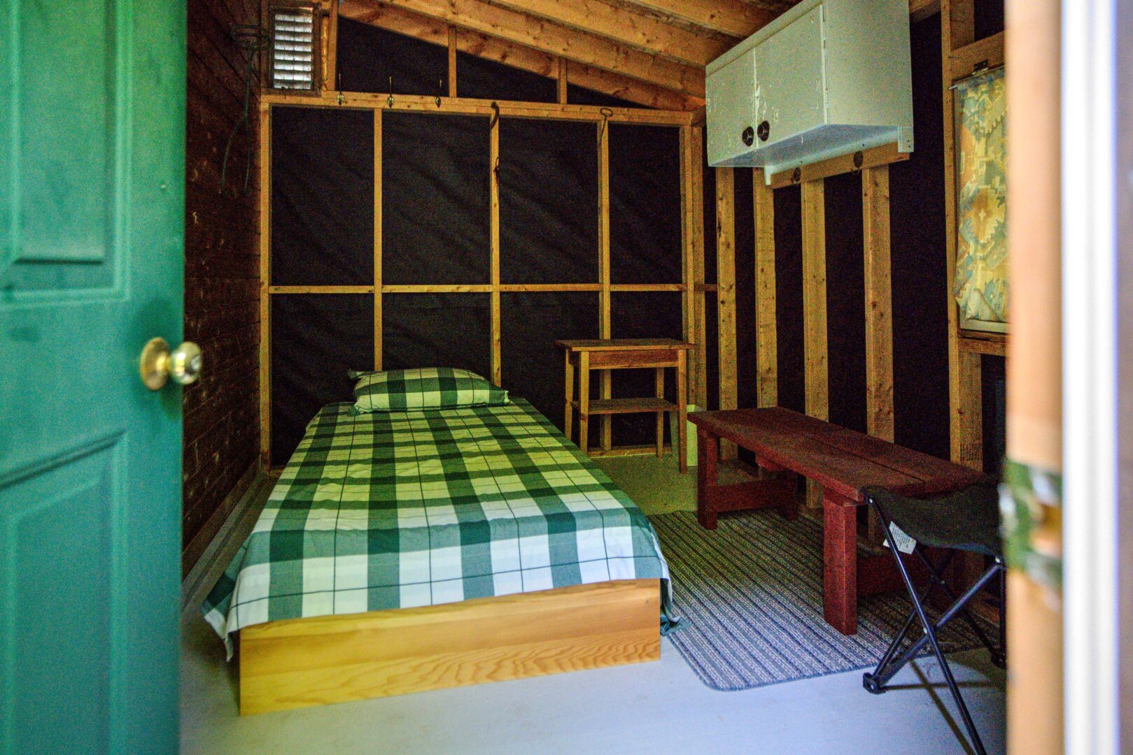 A bed with a green checked bedspread in an unfinished bedroom