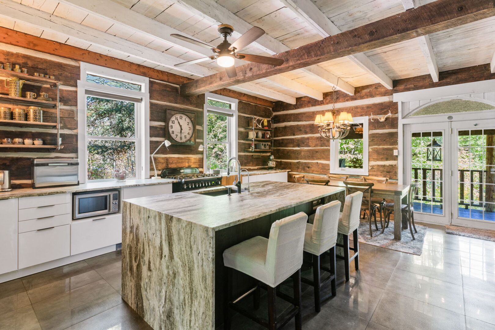Bright log cabin kitchen featuring a granite waterfall island, modern cabinetry, exposed beams, and walkout to deck