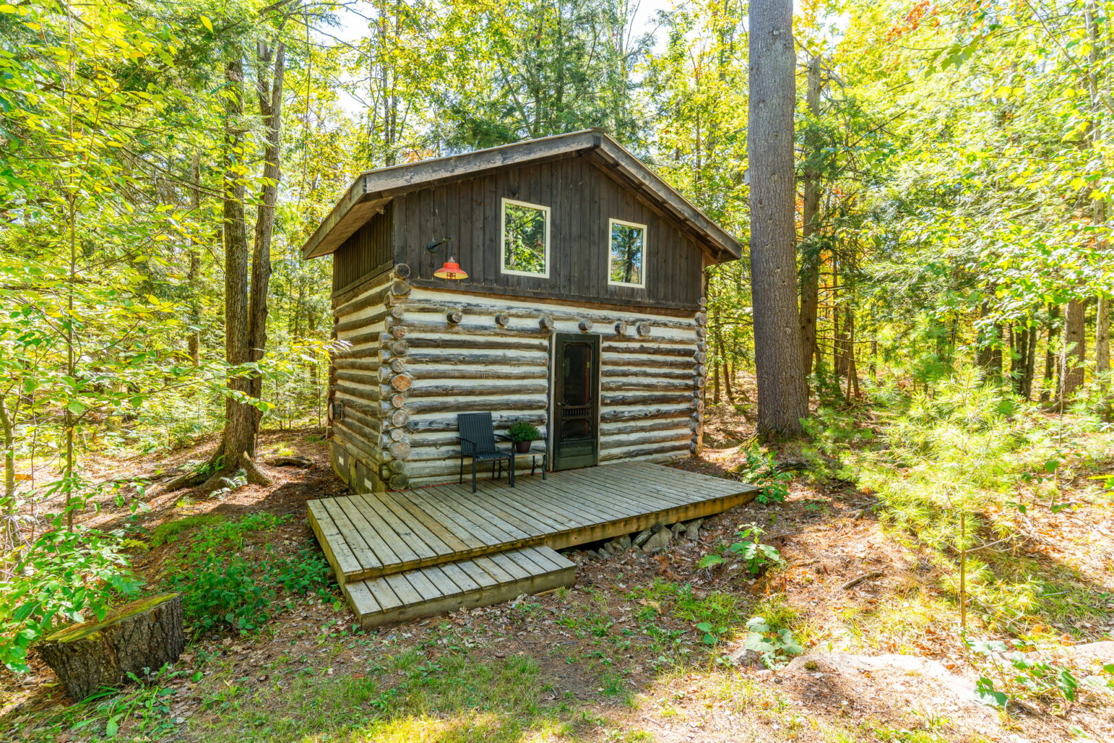 Two-storey log cabin with small front deck, surrounded by forest—ideal for guests, retreats, or quiet escapes