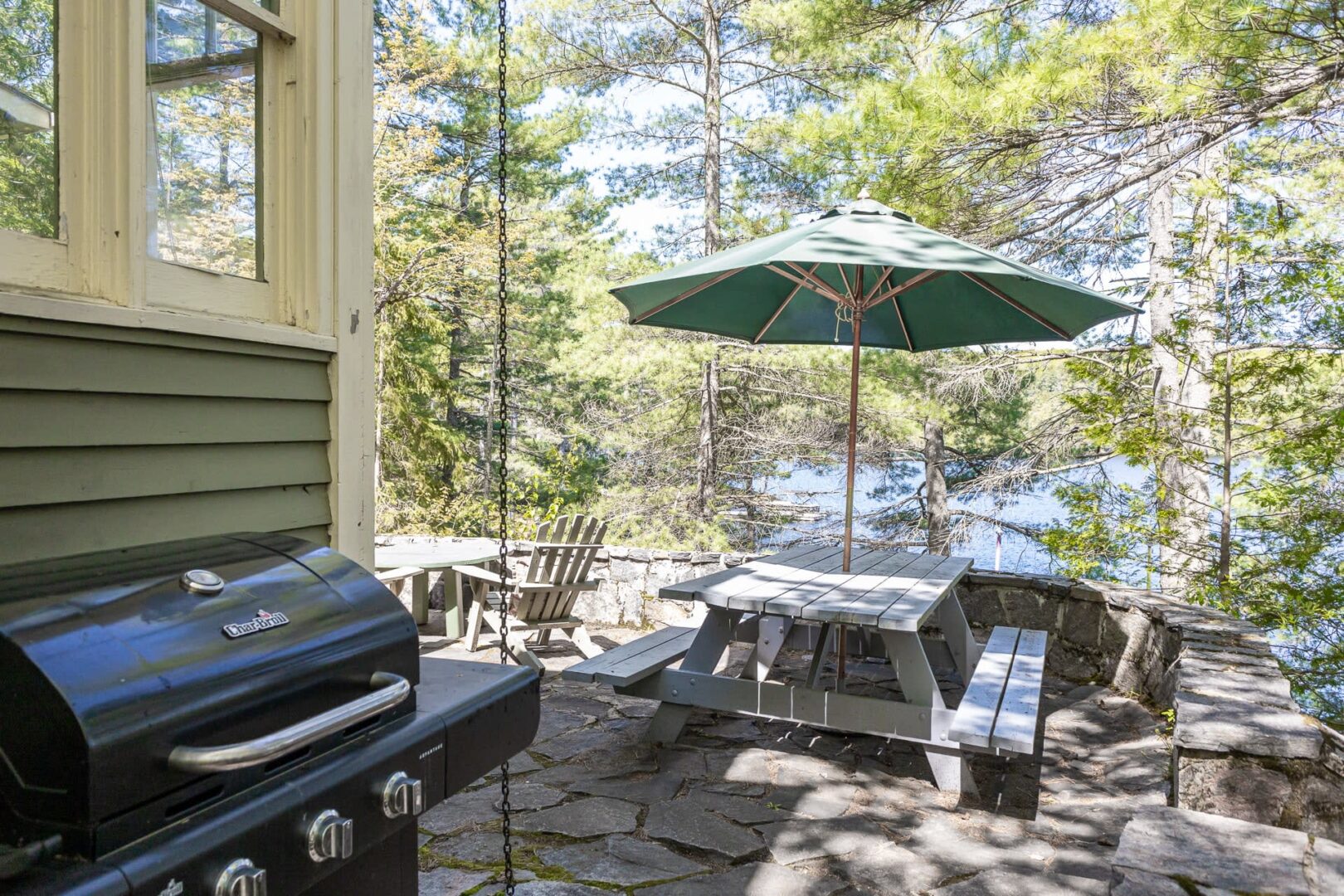 A stone patio with a barbecue, picnic bench and green umbrella