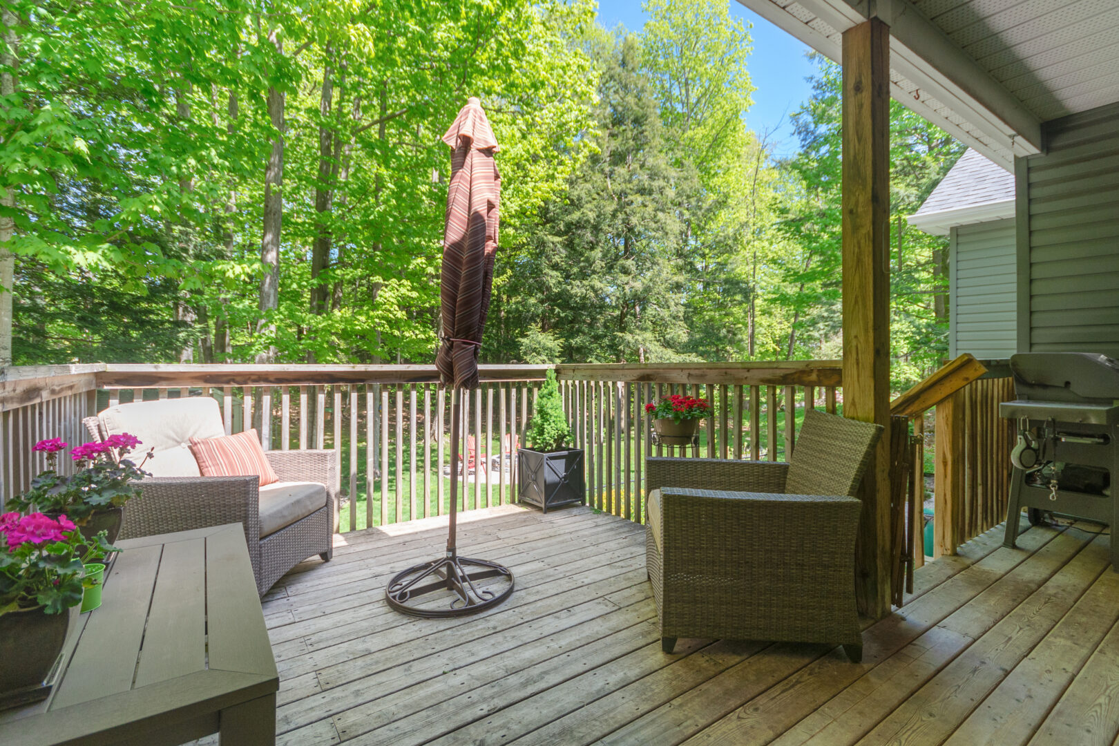 A light wood deck with patio furniture and a closed red umbrella