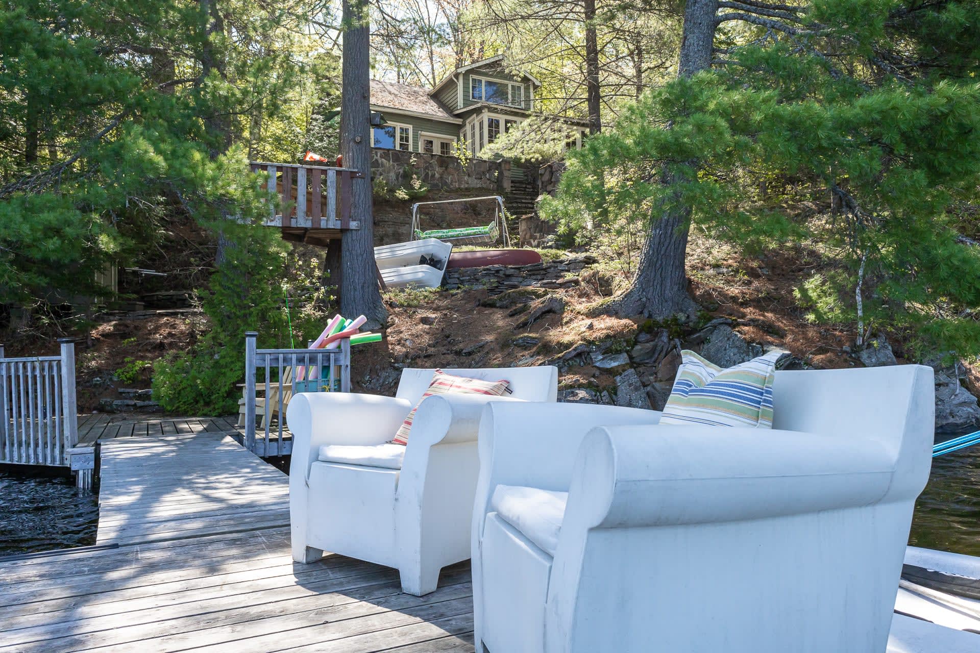 Two white chairs on the dock by a cottage