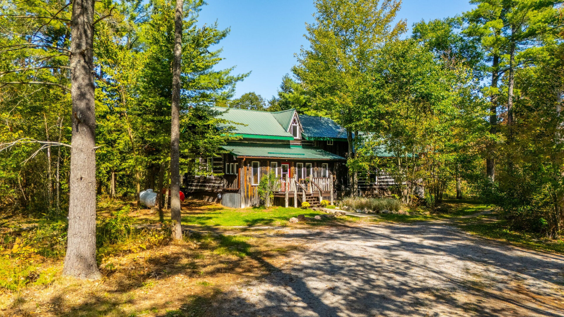 Exterior view of restored 1836 log cabin surrounded by mature trees, featuring green metal roof and front porch