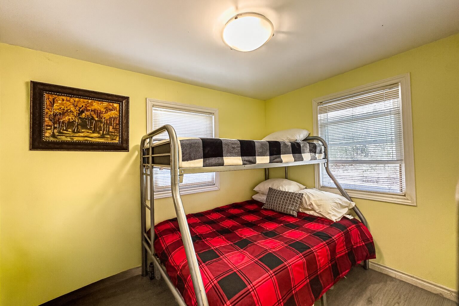 Bunk beds with in a yellow room. the lower bed has a red plaid cover