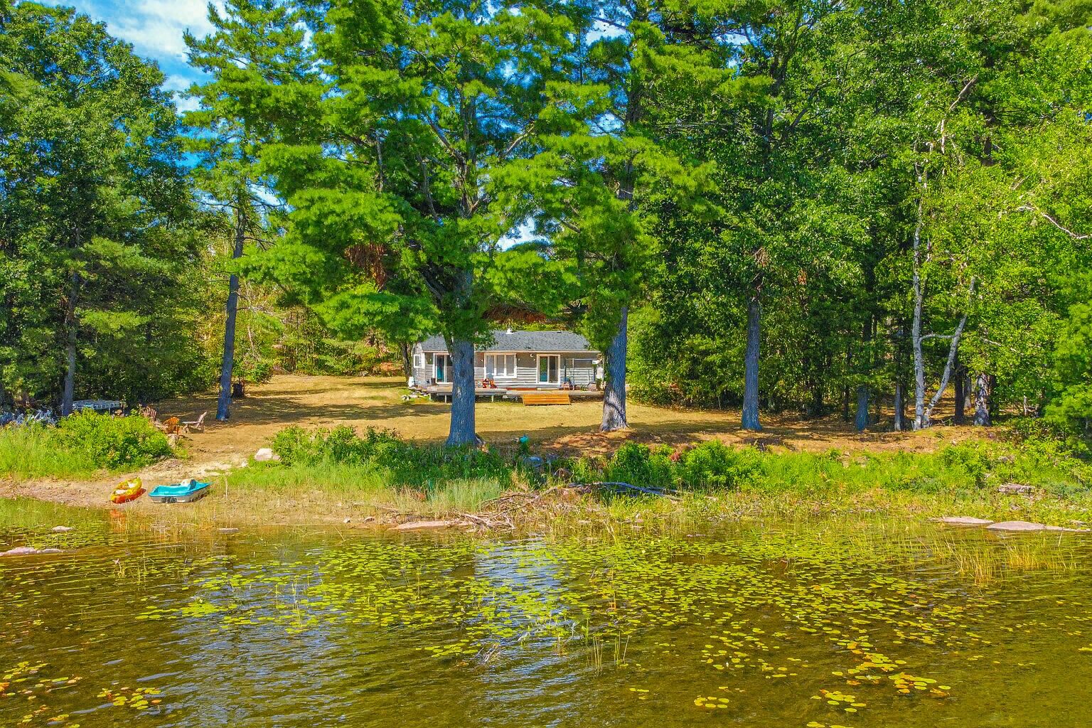 A small grey cottage set back behind trees on a waterfront property