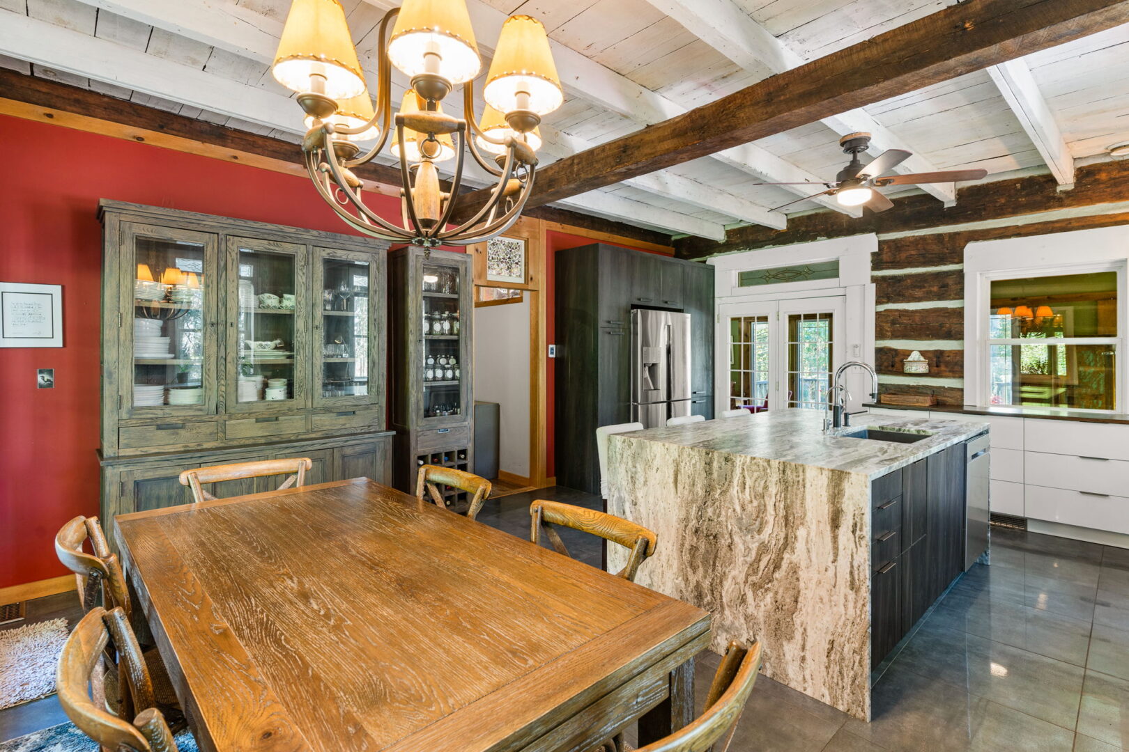 Log cabin dining room featuring rustic wood table, china cabinet, red accent wall, and open kitchen with granite island