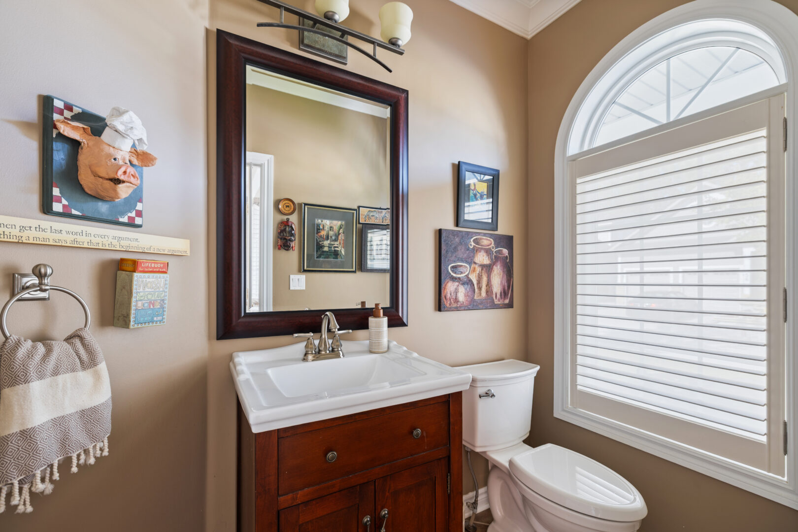 A beige bathroom with a brown vanity and a square mirror
