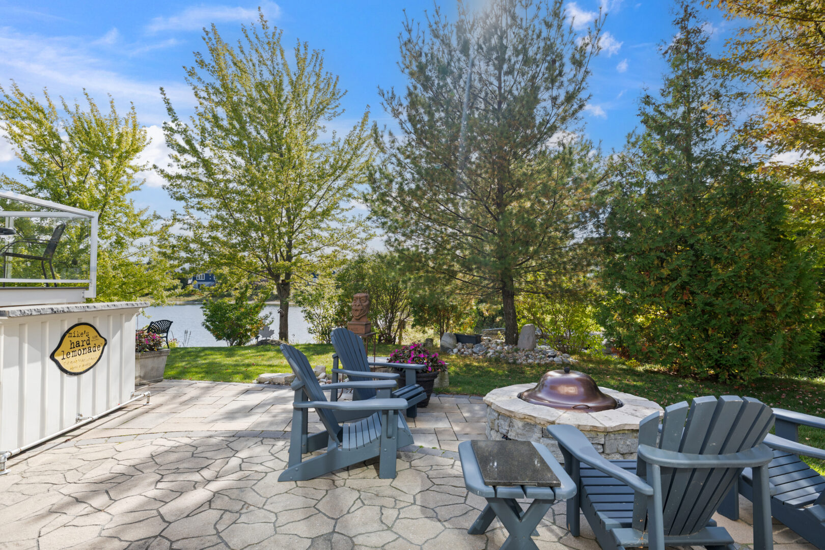 A fire pit surrounded by blue Muskoka chairs on a stone patio