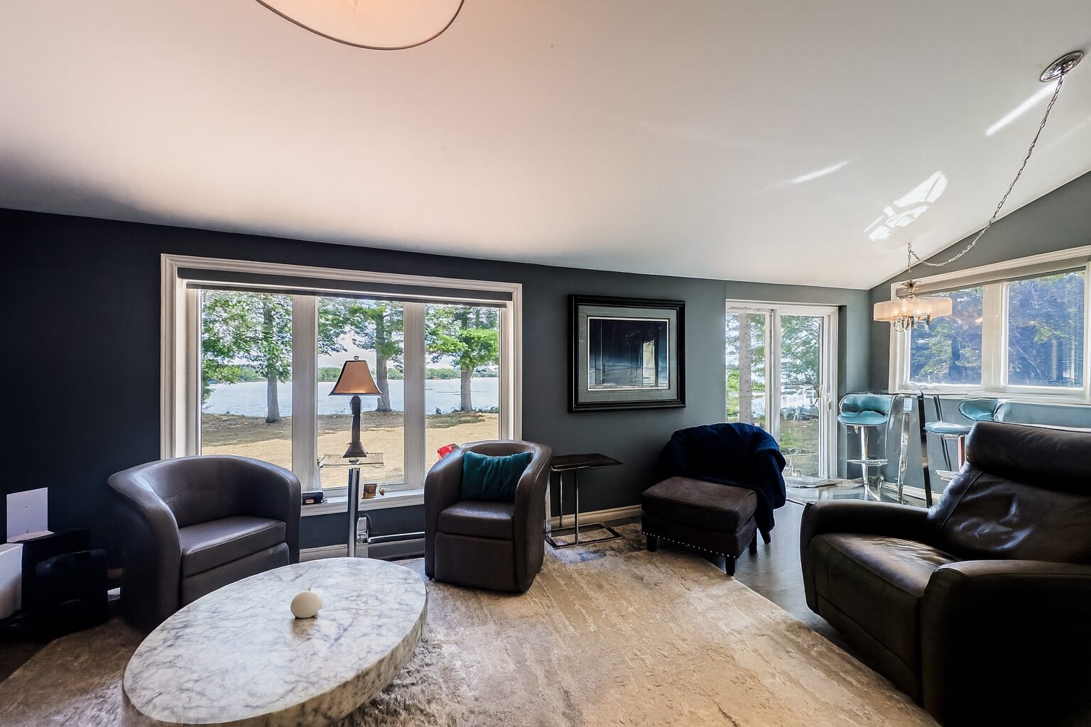 Dark plush chairs face a round coffee table. Behind, glass windows face the lake