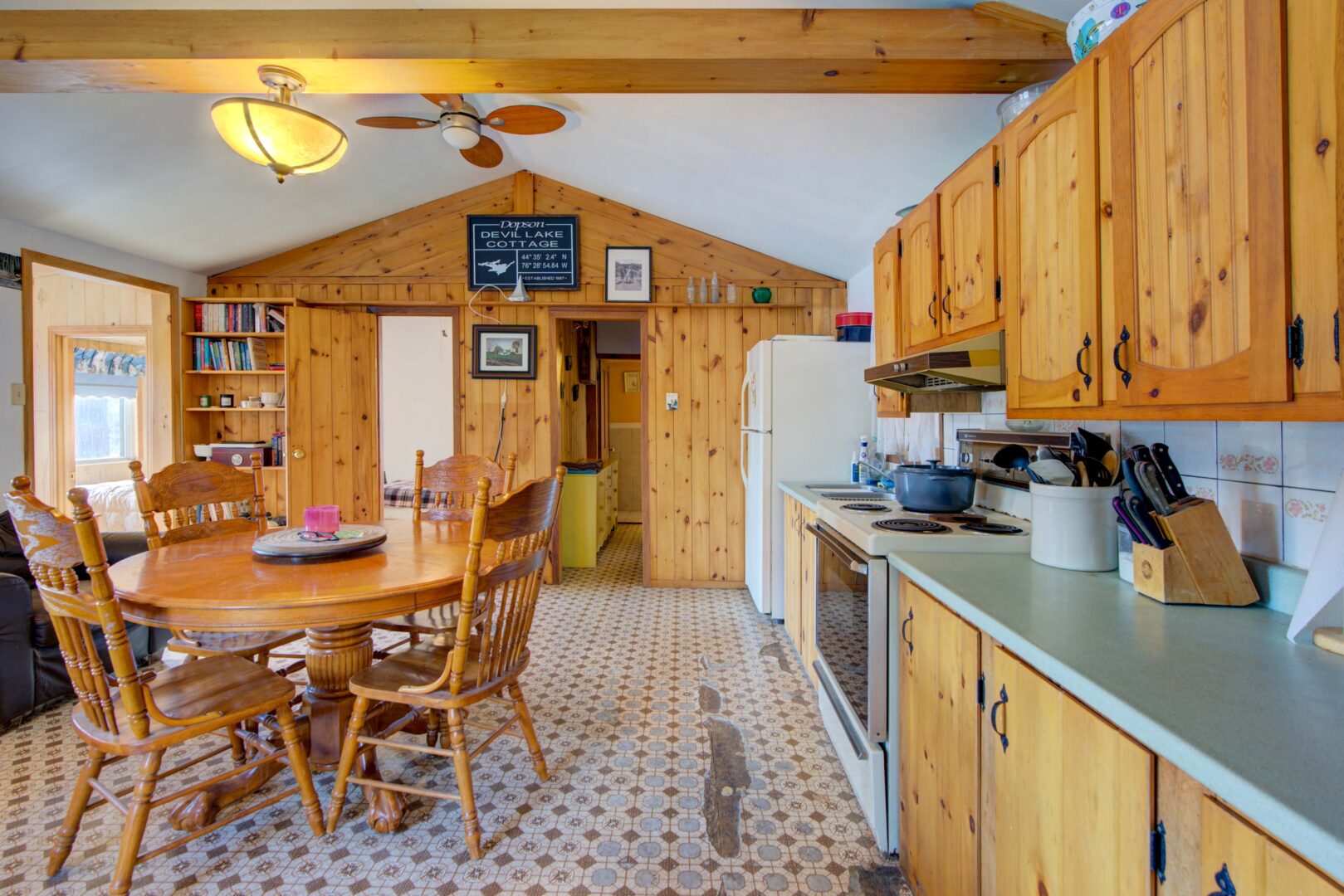 A round wood table in a white kitchen with light wood cabinets and grey-green counters