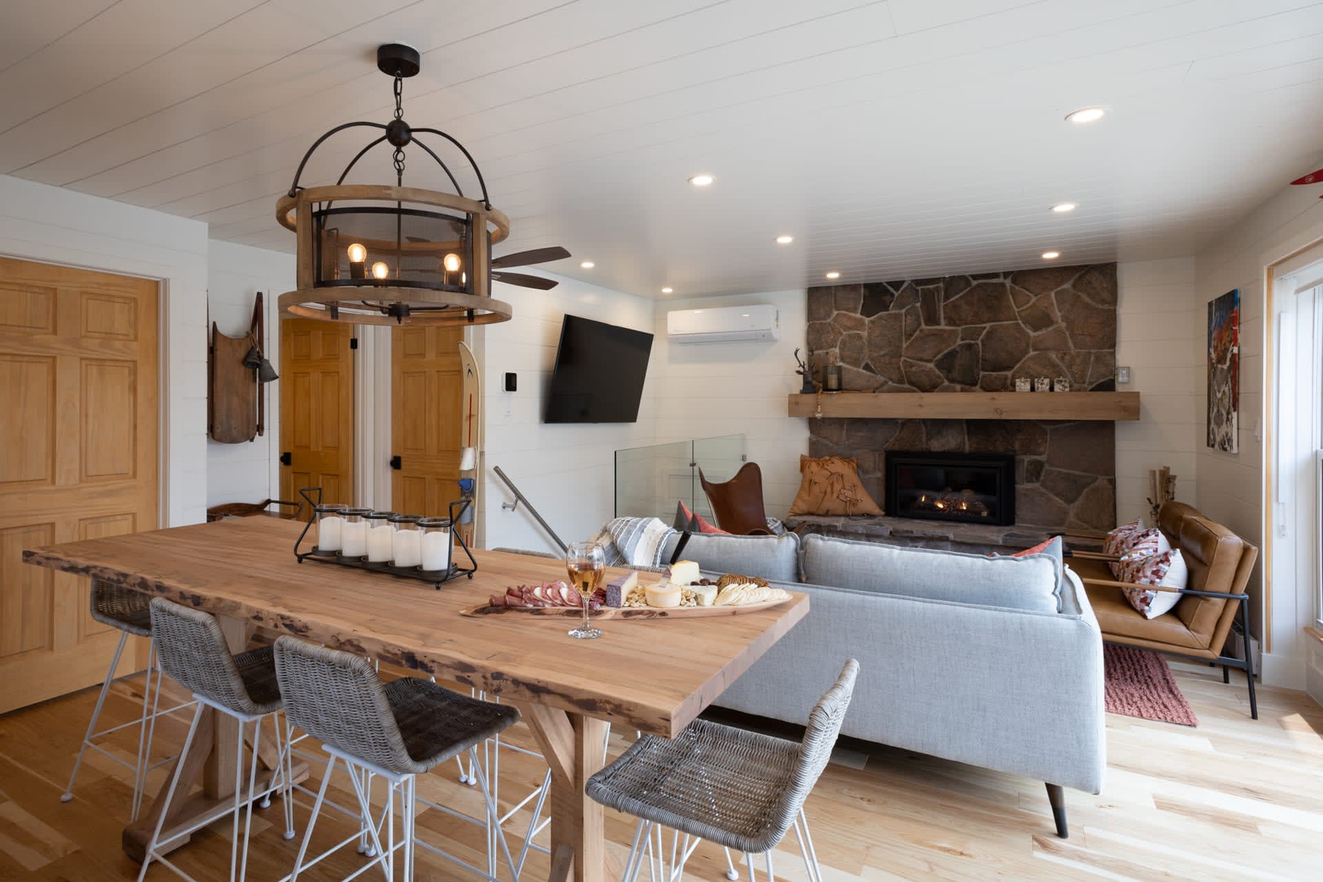 A wood dining table with grey chairs faces a small living small with a granite fireplace