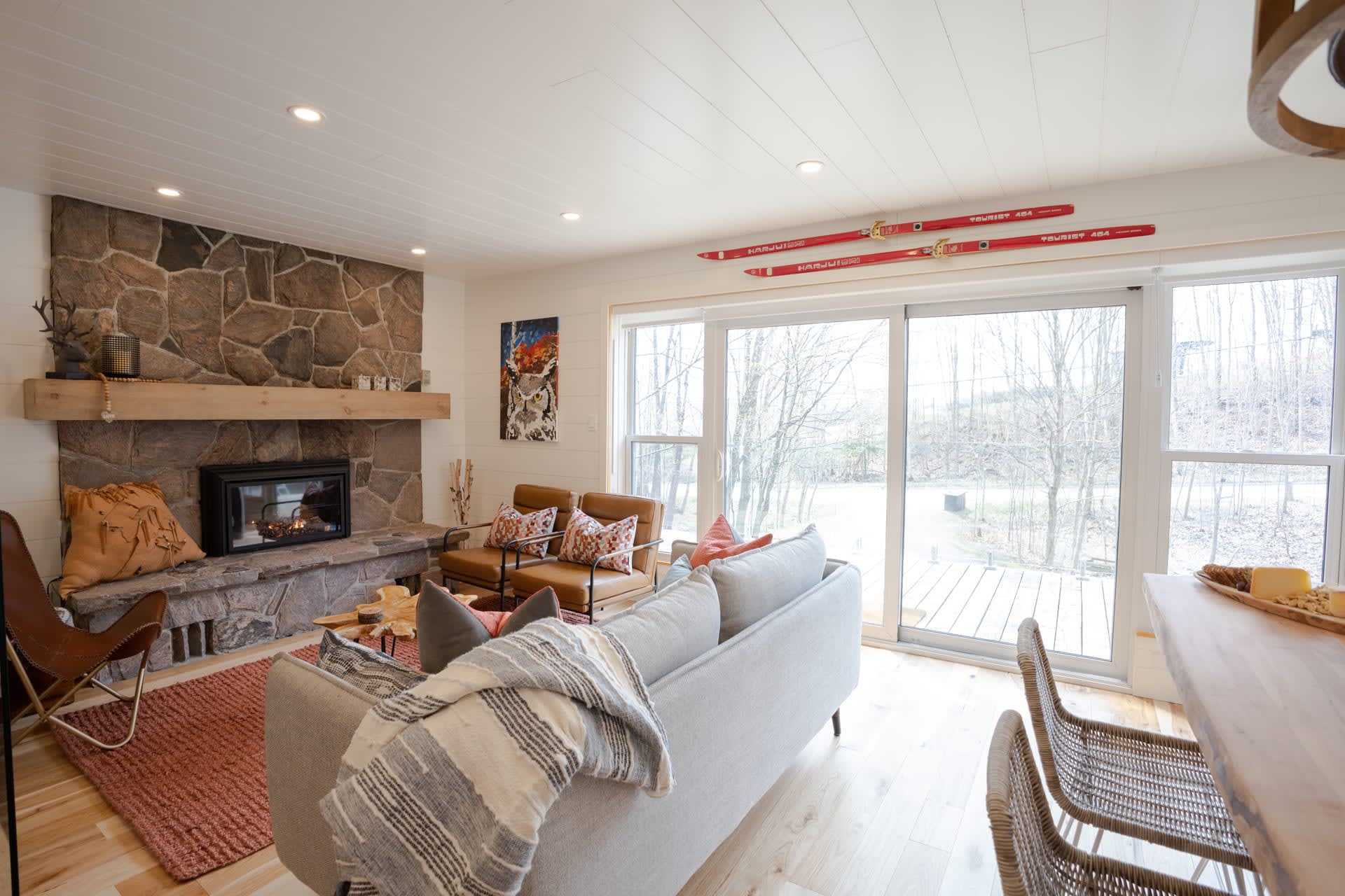 A grey couch with a throw blanket tossed over the back faces a granite fireplace. To the right, bright windows that face the yard