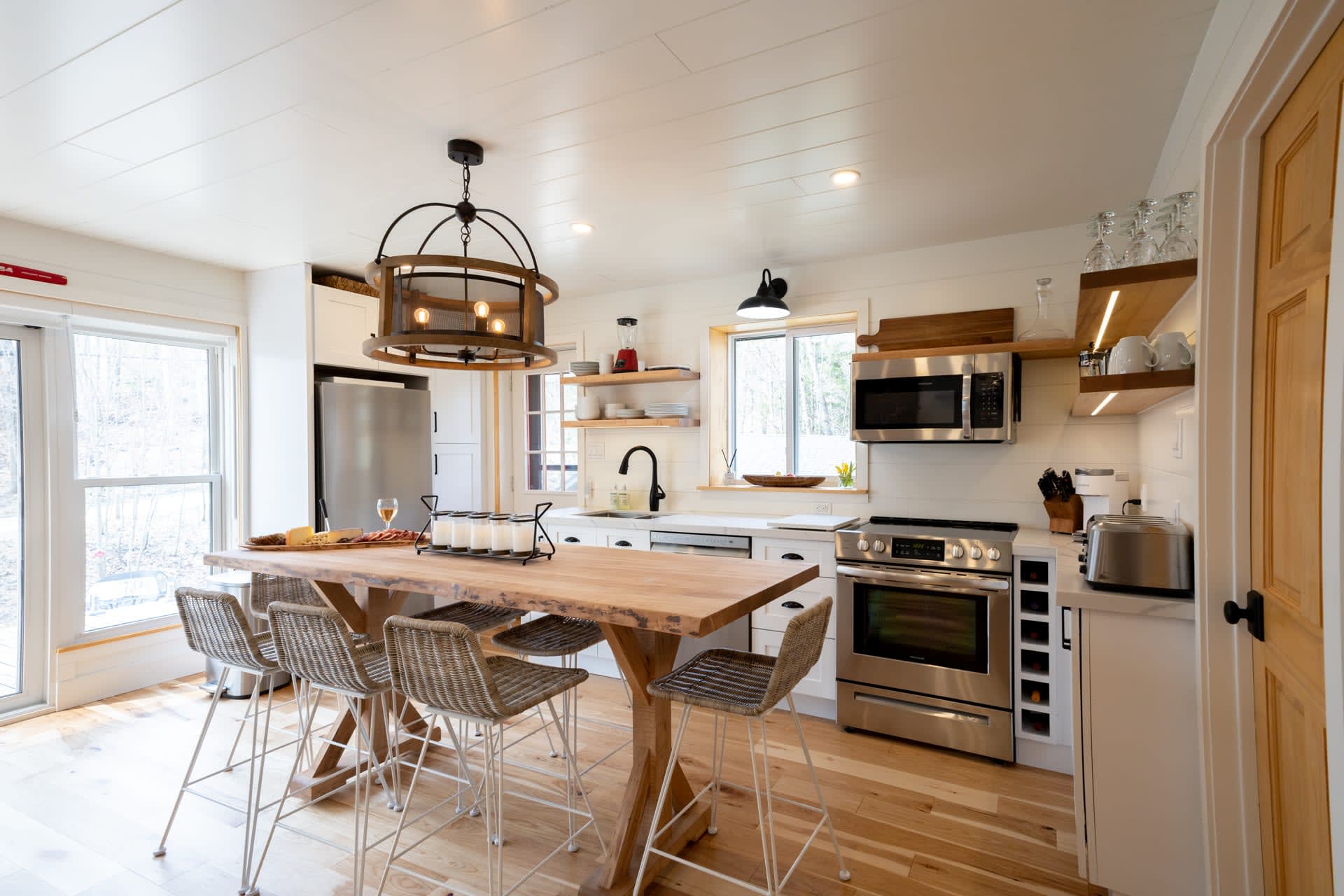 A white kitchen with stainless steel appliances along the back wall, a wood dining table and grey chairs