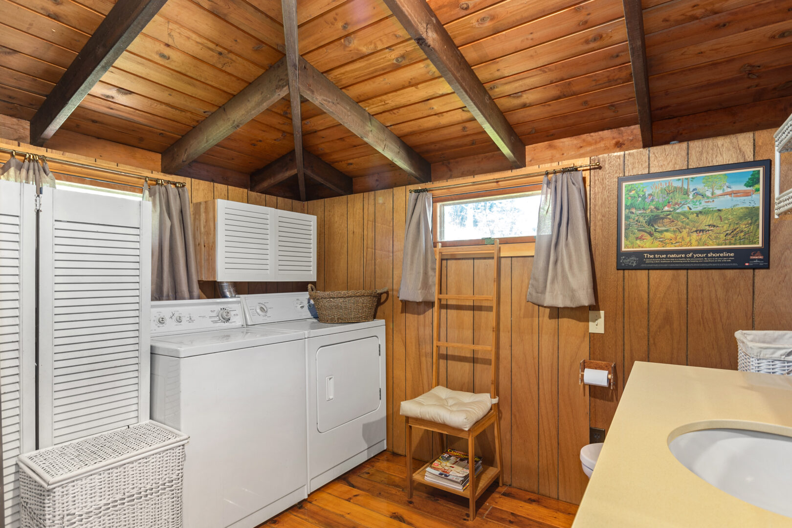 White laundry machines face a vanity and toilet in a wood paneled bathroom