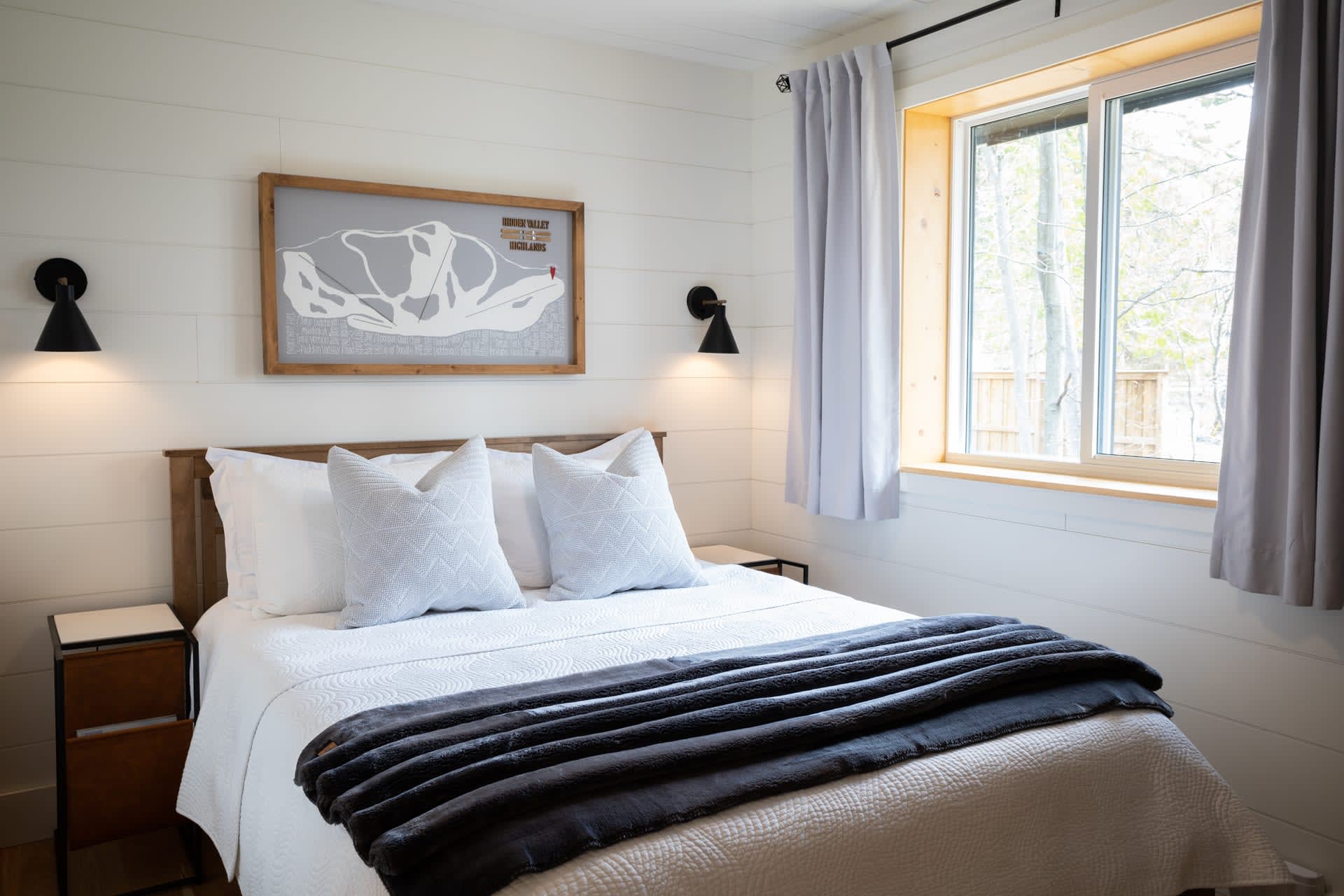 A white bed with a dark grey blanket at the end in a white bedroom