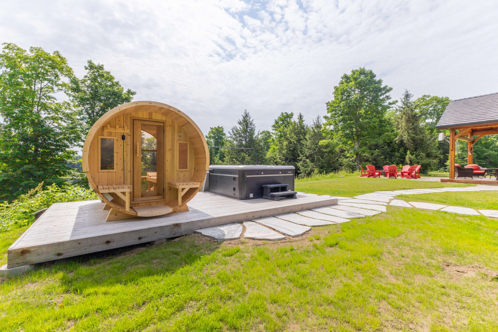 A barrel sauna sits on a raised platform next to a covered hot tub