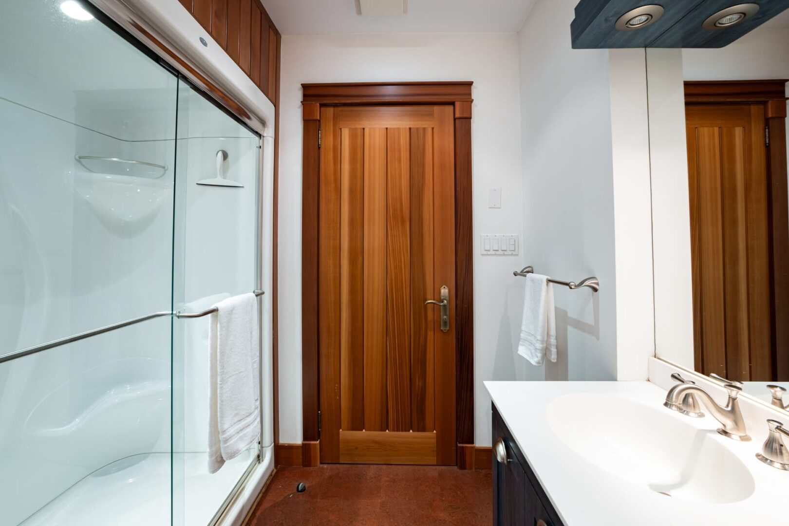 A white bathroom with a wood door and wood floors