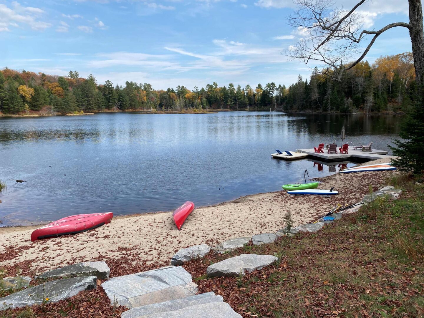 A sandy beach on a lake with red kayaks laying face down