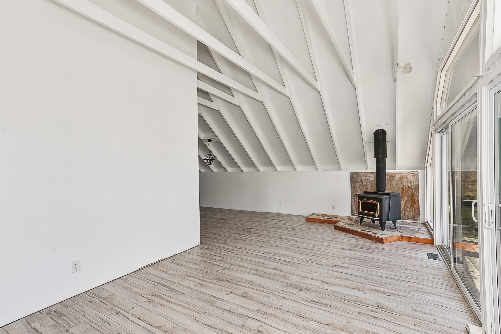 A white living area without furniture. A wood stove sits in the corner