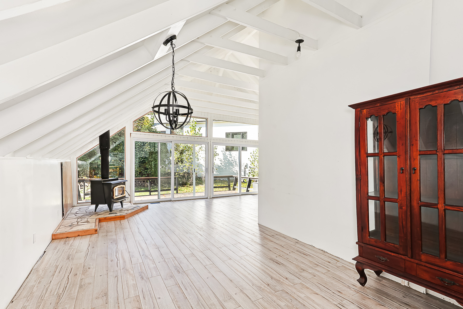 A white living area with a wood stove tucked by sliding glass doors and vaulted ceilings