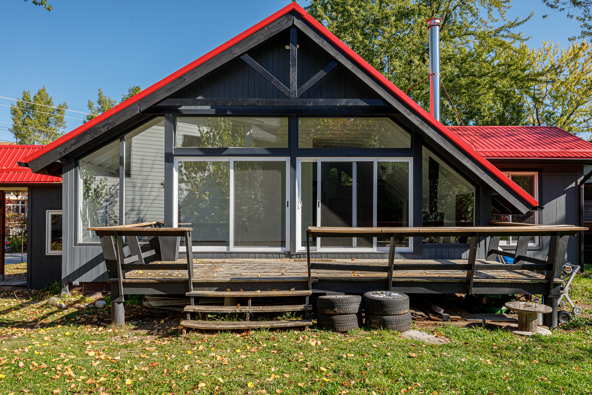 An A-frame cottage with a red roof, sliding glass doors and a deck
