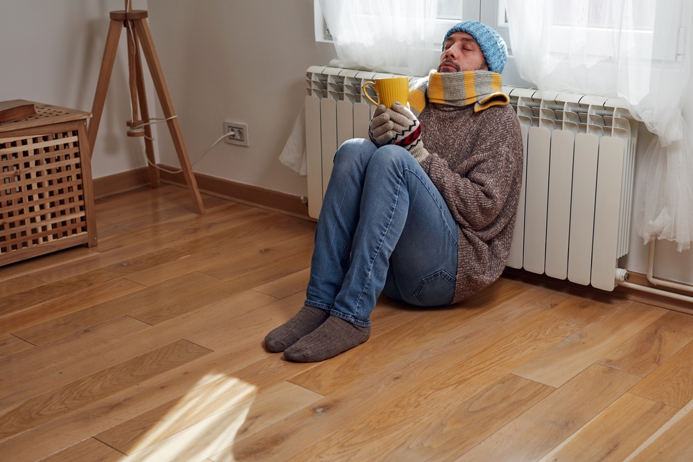 A man huddled at a thermostat