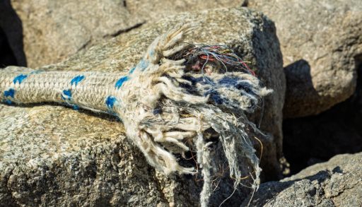 Close-up of a frayed end of a boating rope sitting on a rock